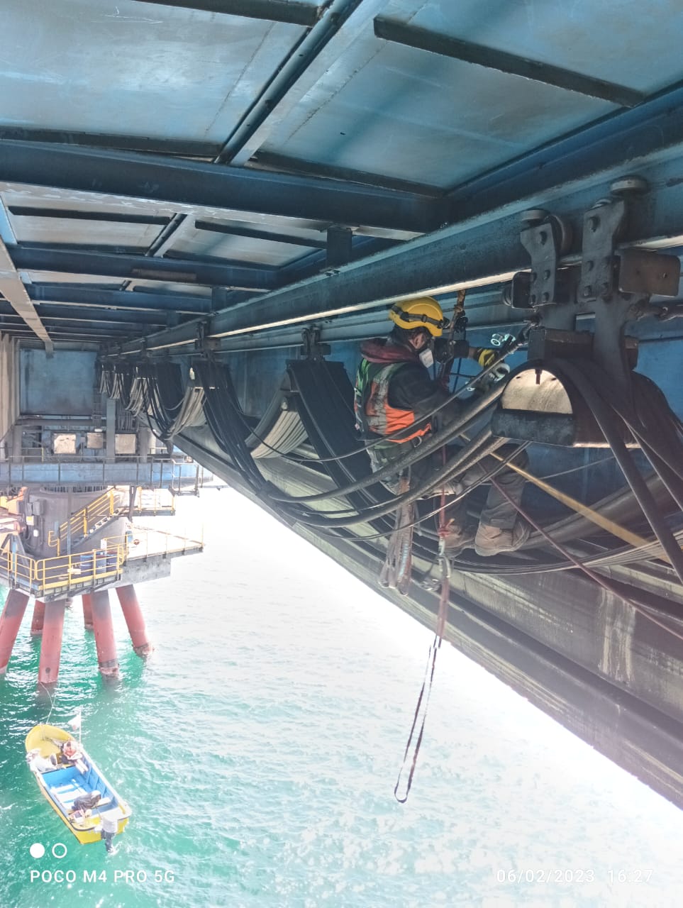 Operador de AMS suspendido por cuerda bajo el cargador de barcos del puerto de Totoralillo, a más de 20 metros sobre el mar turquesa